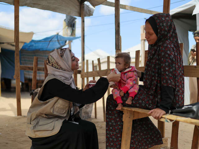 RESCUE:s medarbetare matar ett litet barn i Gaza med nötkräm mot undernäring. Barnet sitter i sin mammas knä.
