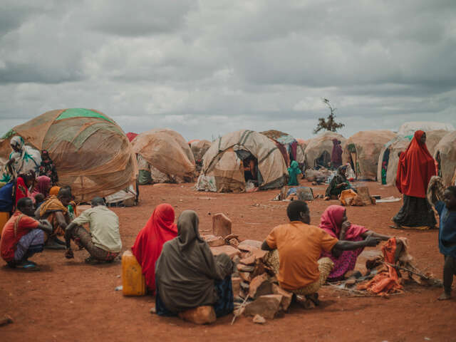Människor sitter på marken i ett flyktingläger och lagar mat.