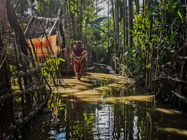 En kvinna vadar i vatten och visar upp sin bostad som blivit förstörd efter en översvämning.