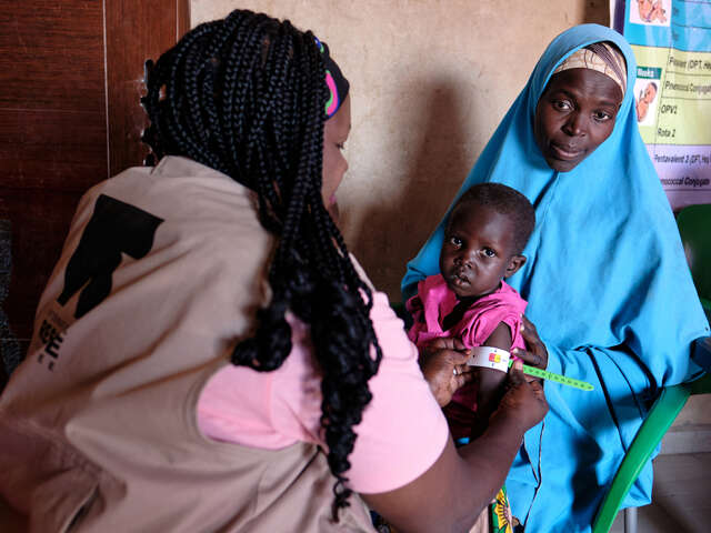 En mamma sitter med ett litet barn i famnen som undersöks för symptom på undernäring.