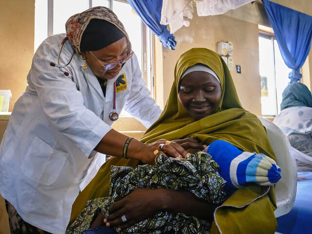 En läkare undersöker ett spädbarn som ligger i sin mammas knä.