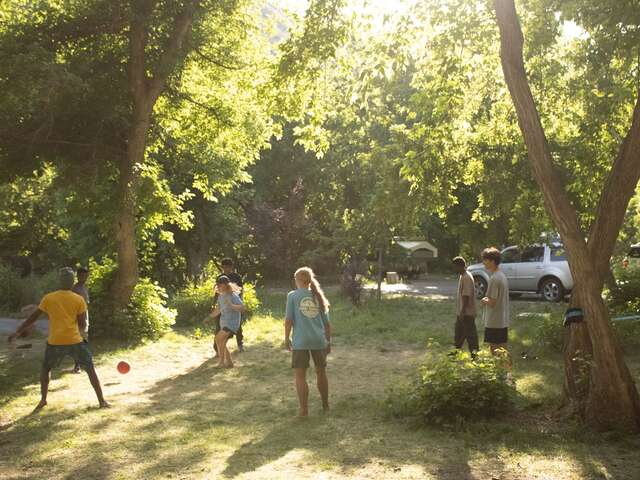 Refugee youth and Summit Journeys team members play soccer in a shady, wooded area.
