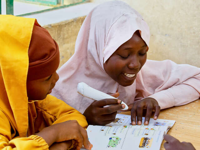 Två flickor i Nigeria sitter böjda över en lärobok och studerar.