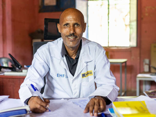 En man som är rektor för en skola i Etiopien sitter vid sitt skrivbord och ler mot kameran.