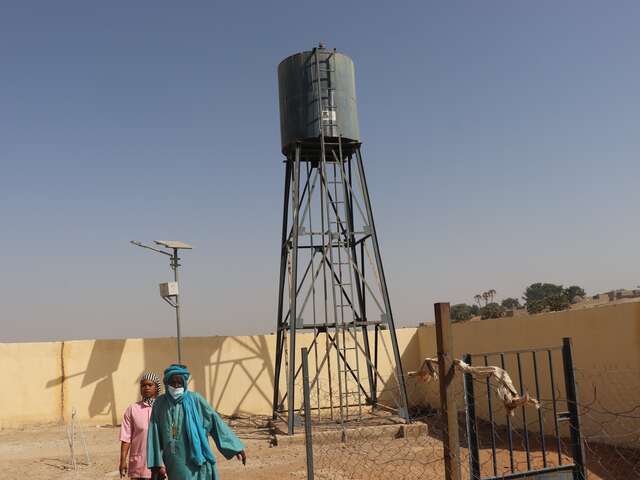 Tula and Oumarou explain the solar-powered water tower that keeps the health centre running. The water is pumped and stored in an elevated tank, ready to be used for handwashing, hygiene, and medical care—without relying on unstable power grids.