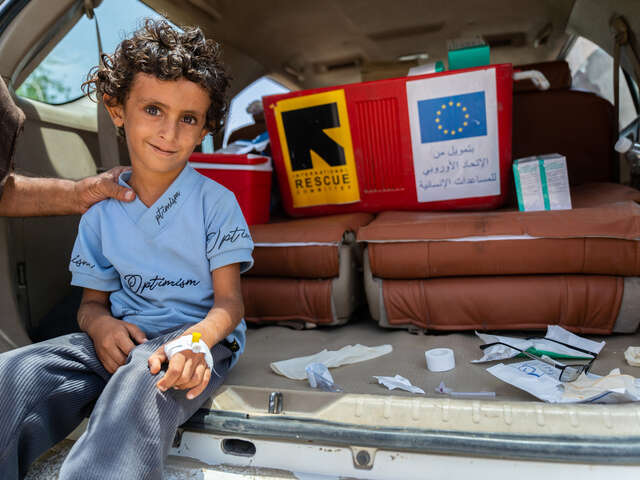 En pojke i Jemen ler och har fått bandage om handen. Han sitter i bakluckan på en av RESCUE:s hälsobilar l som är lastad med läkemedel och medicinsk utrustning.