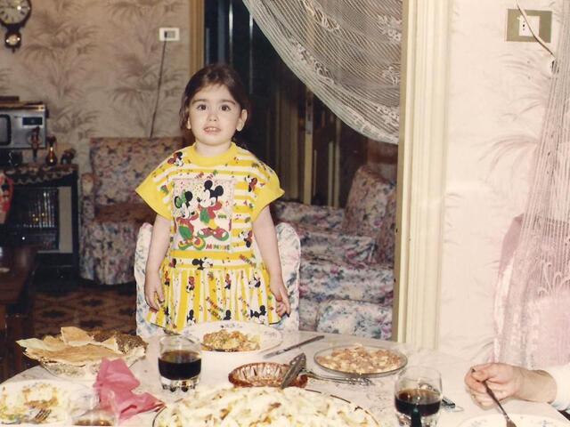 Dressed in festive clothing, Mariela stands at a table filled with edible treats 