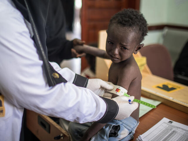A health worker at an IRC-supported clinic in Sana'a, Yemen, measures a young boy's arm to confirm he is suffering from malnutrition.