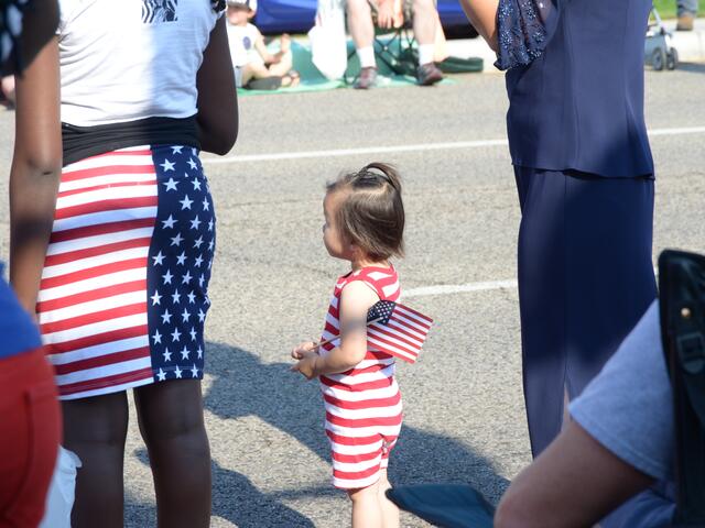 Toddler watching fourth of July parade with United States flag in hand.