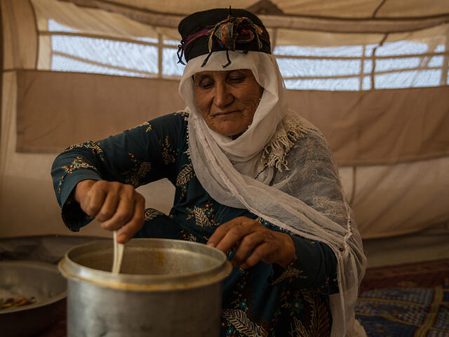 An Afghan woman stirs food in a pot while sitting in a tent in a refugee camp