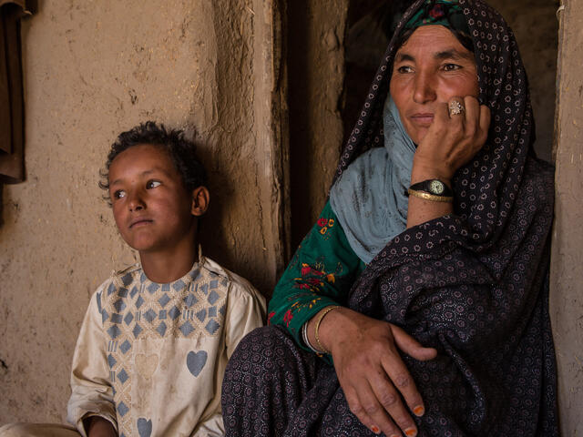 A mother sits against a wall next to her 7-year-old son.