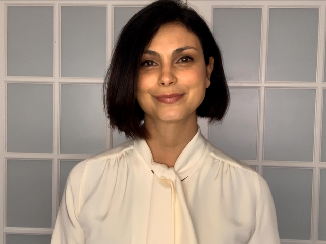 Wearing a white blouse, Morena Baccarin looks at the camera