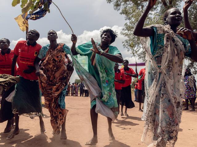 Outside, several women dance with their arms in the air. 