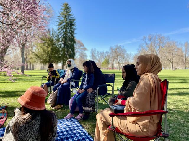 Four women, some with children on their laps, sitting in lawn chairs outside at a park in early spring discussing mental health with the International Rescue Committee health team.