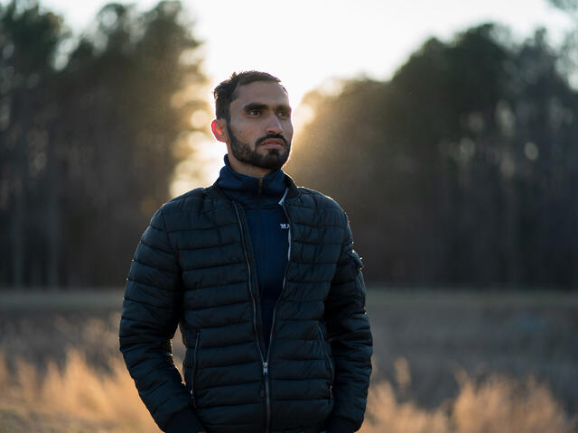Photojournalist Mohammad Anwar Danishyar stands in front of a forest in the evening.
