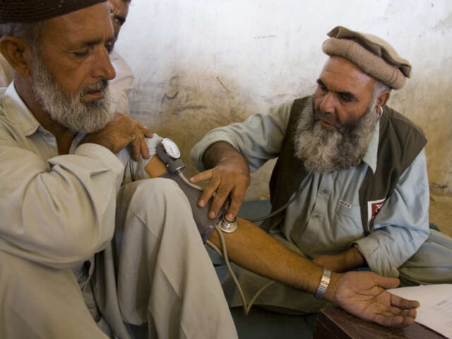 En läkare och en man sitter på golvet och läkaren undersöker mannen.