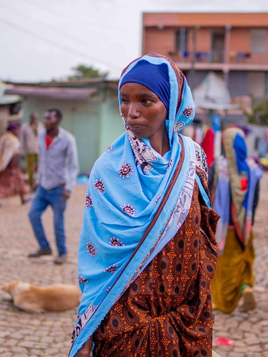 파란색 머리 스카프를 두른 한 여성이 에티오피아 데데르의 시장을 걷고 있습니다.