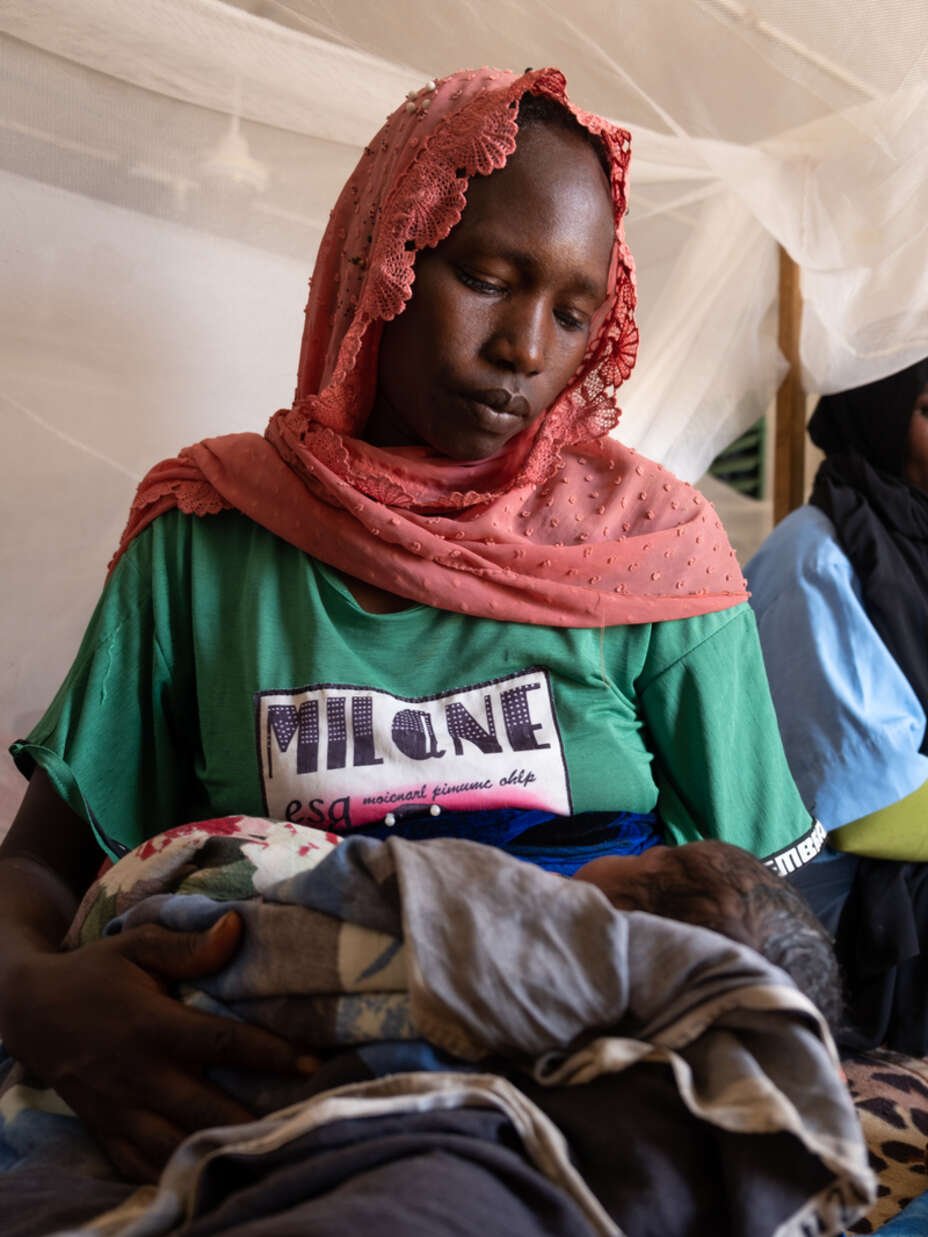 Nybliven mamma i Tchad sitter med sin bebis i famnen i en säng.