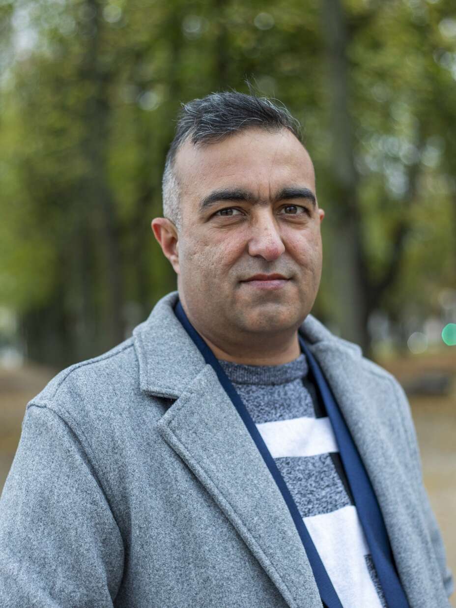 Porträt eines Mannes aus der afghanischen Gemeinschaft in Deutschland, aufgenommen in einer ruhigen Parkumgebung.