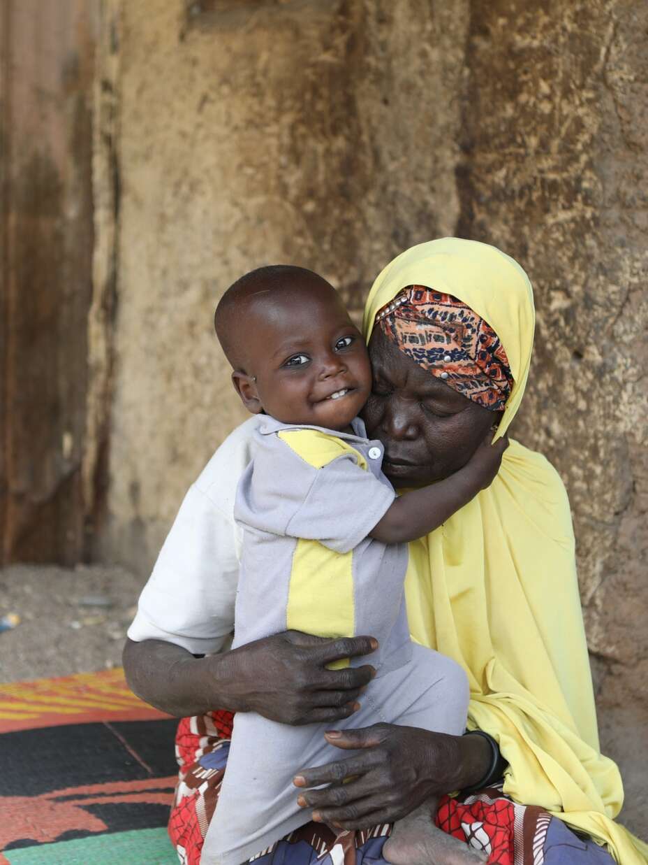 나이지리아의 한 할머니가 국제구조위원회 치료 센터에서 영양실조 치료를 받은 손자를 집 밖에서 안고 있습니다.