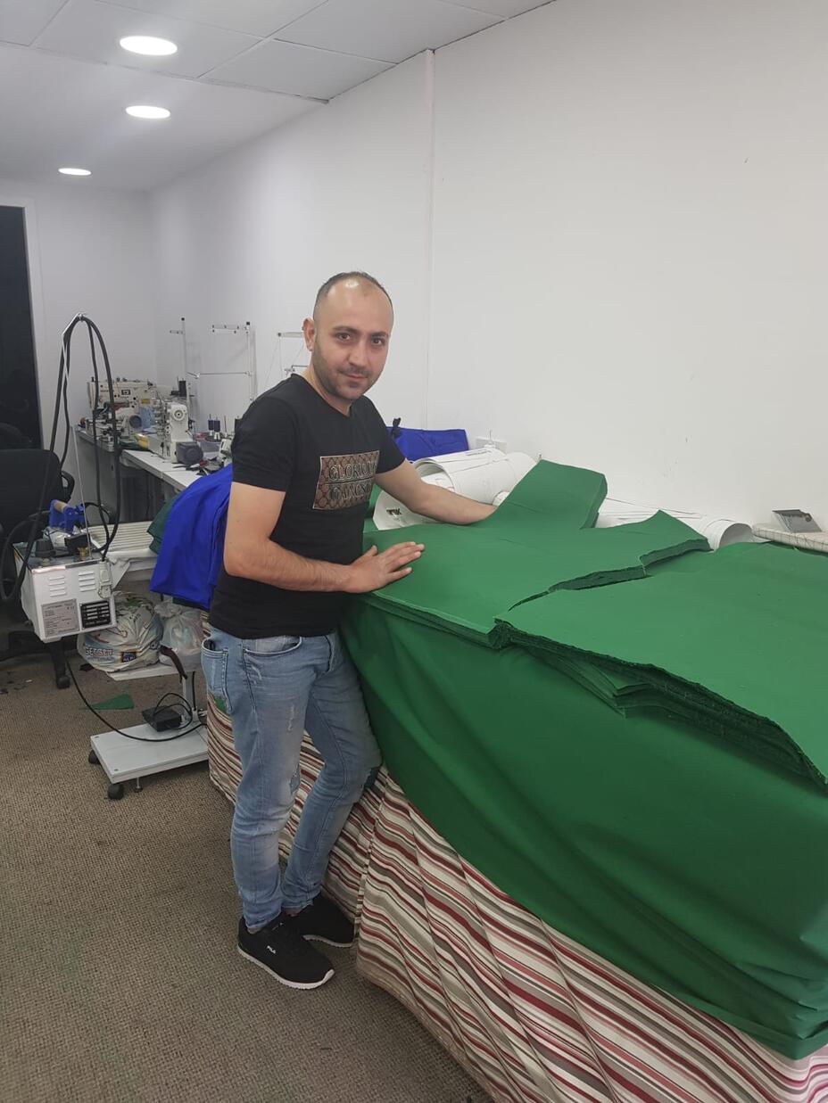 Jehad Haji Rechad stands in his tailors shop next to scrubs he's cut for NHS hospital workers.