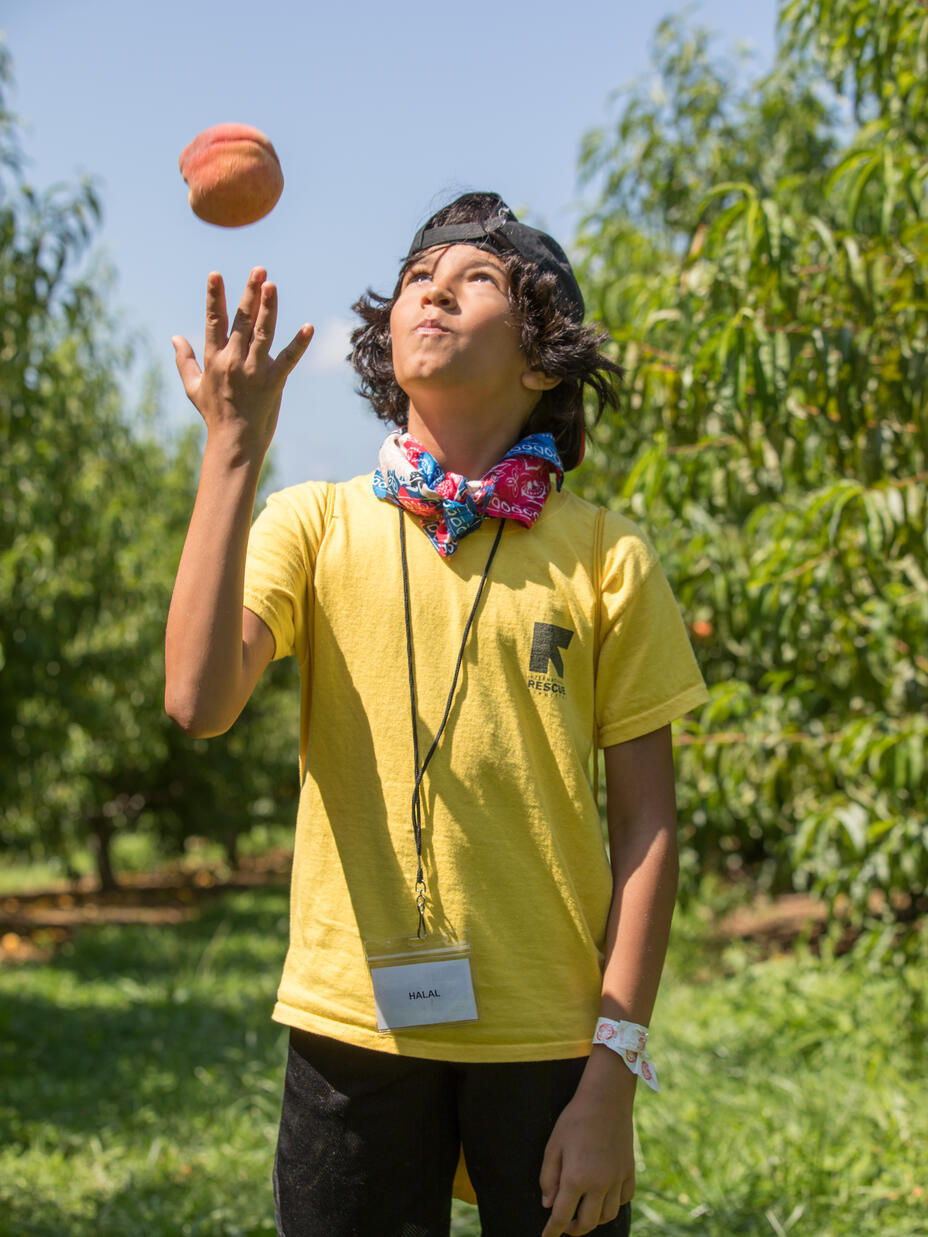 RYSA student wearing a cap and a RYSA shirt, enjoying peach picking and throwing it in the air.