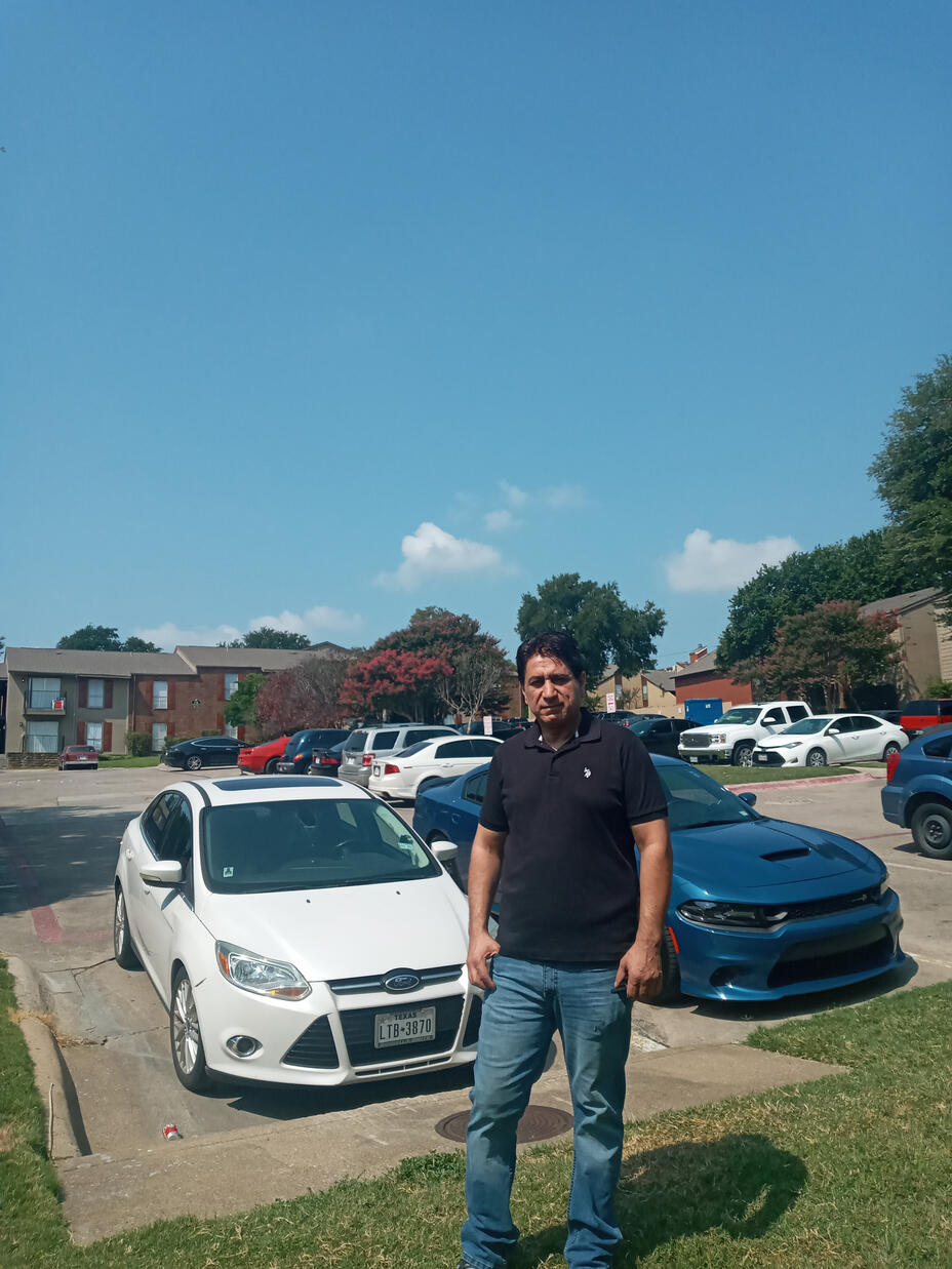 Ehsanullah stands in front of a parking lot and apartment complex