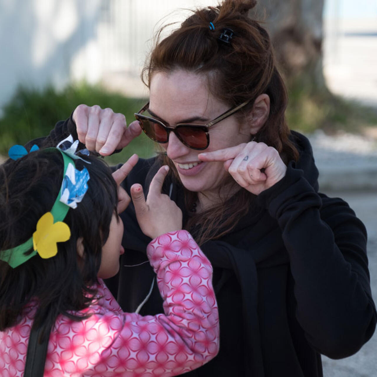 Eine Frau mit Sonnenbrille albert mit einem kleinen Mädchen herum.