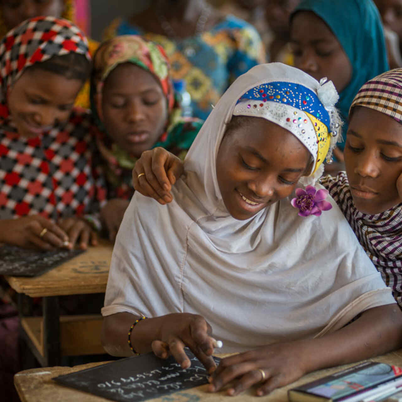 Mädchen sitzen in einem KLassenzimmer an einem Pult und reden mit einander