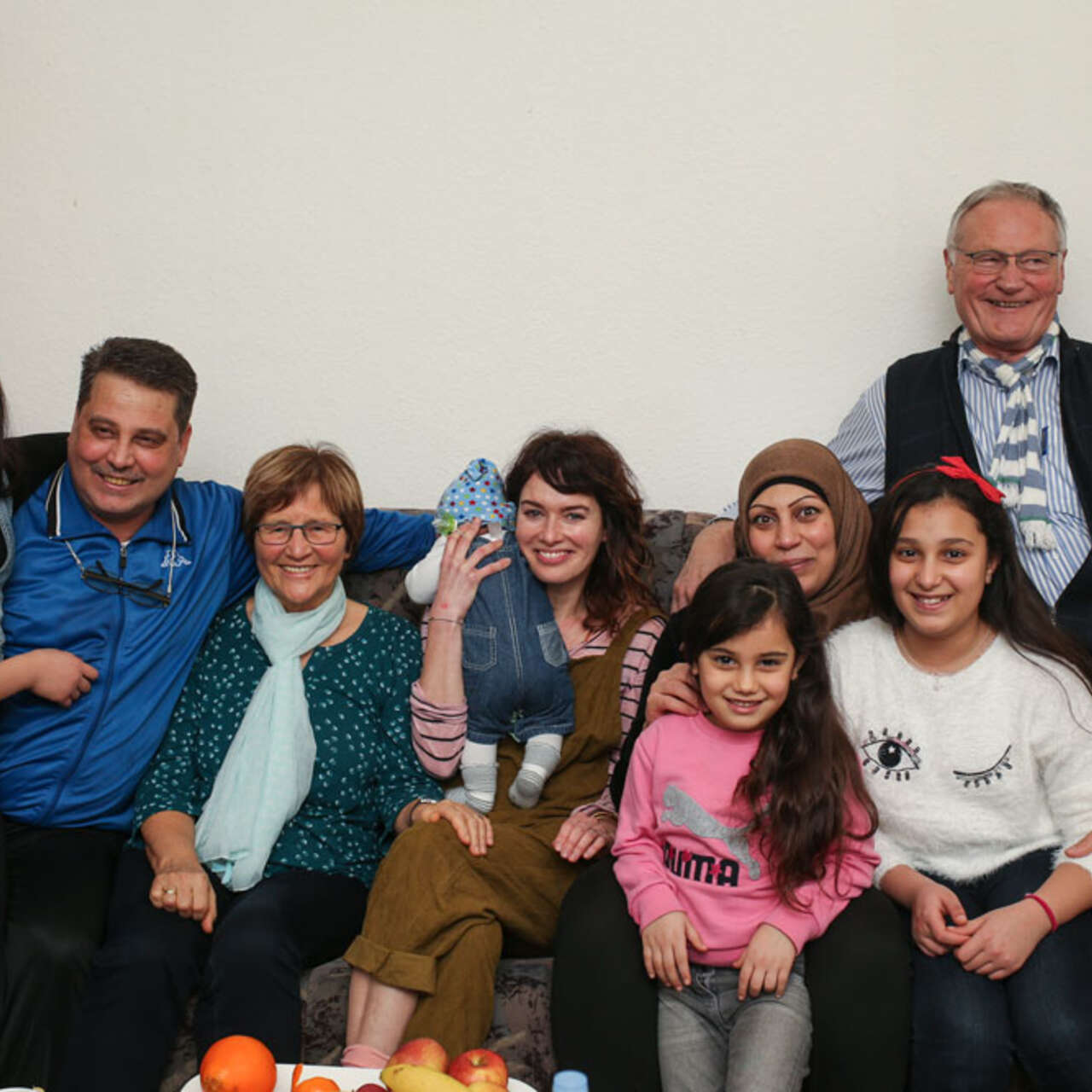 Viele Memschen sitzen auf einem Sofa und alle lächeln in die Kamera