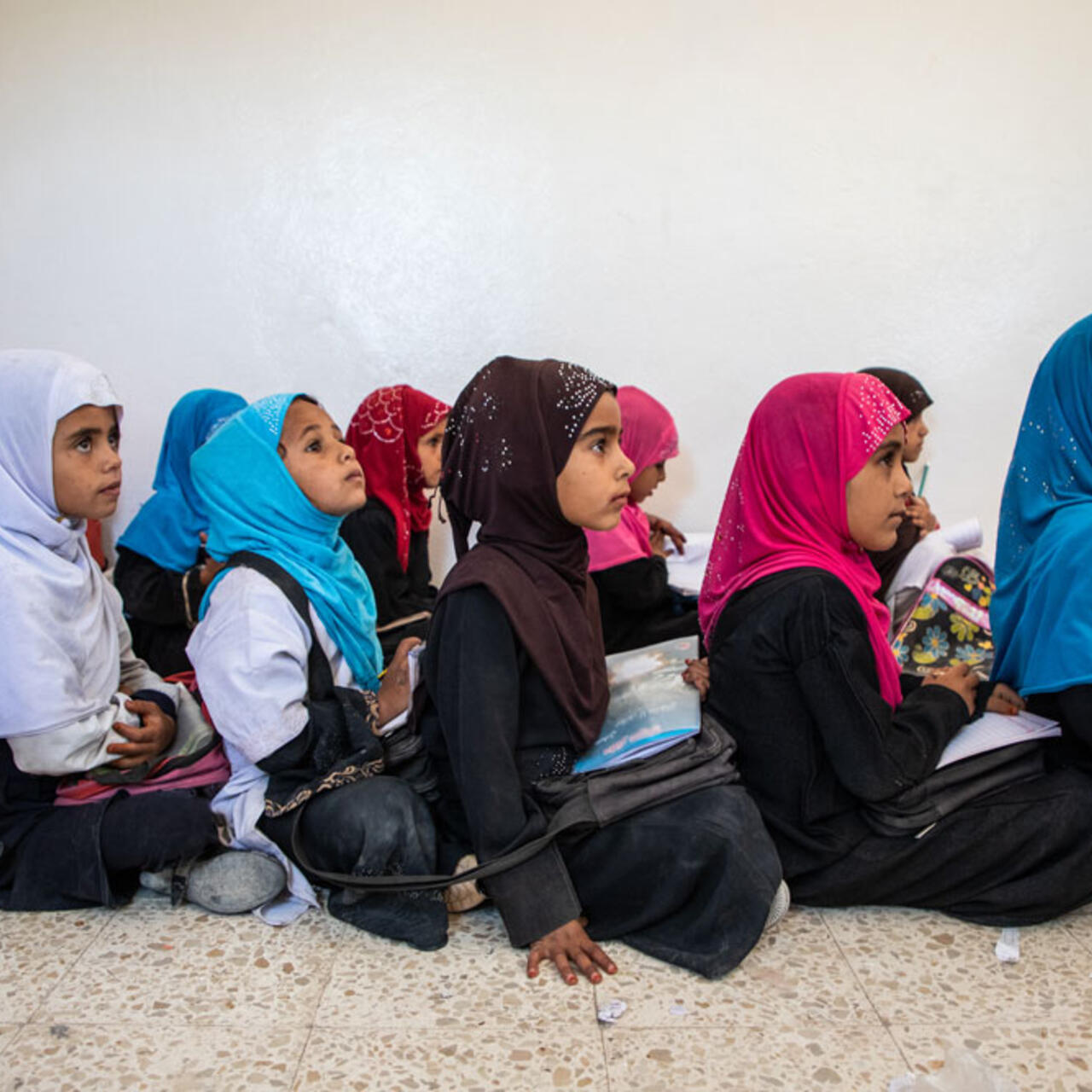 Viele junge Mädchen, mit bunten Kopftüchern sitzen auf dem Boden in einer Reihe