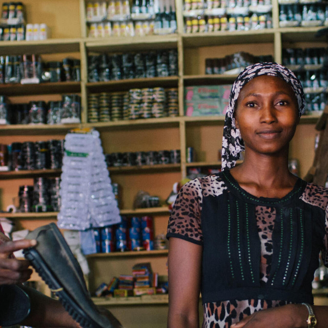 Lydia sitzt mit einem Mann in ihrem Schuhgeschäft. Im Hintergrund sieht man viele Schuhe in den Regalen stehen.