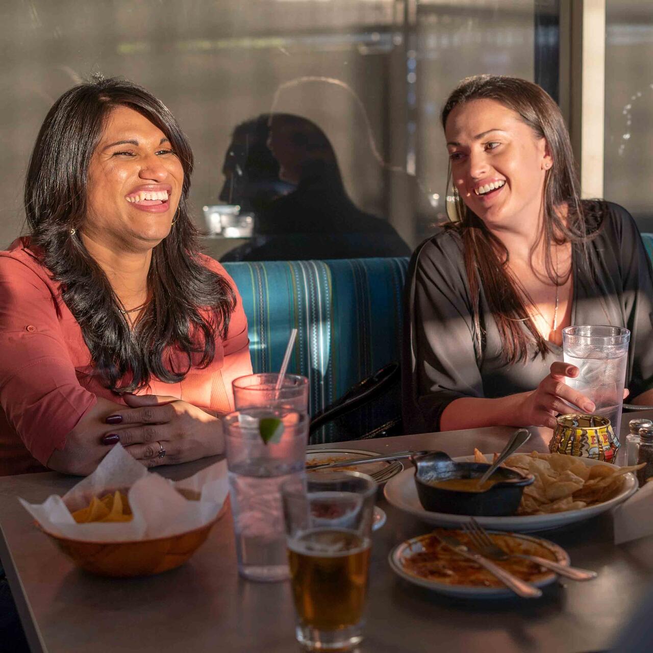 Zwei Frauen sitzen in einem Cafe und lachen herzlich in Phoenix, Arizona