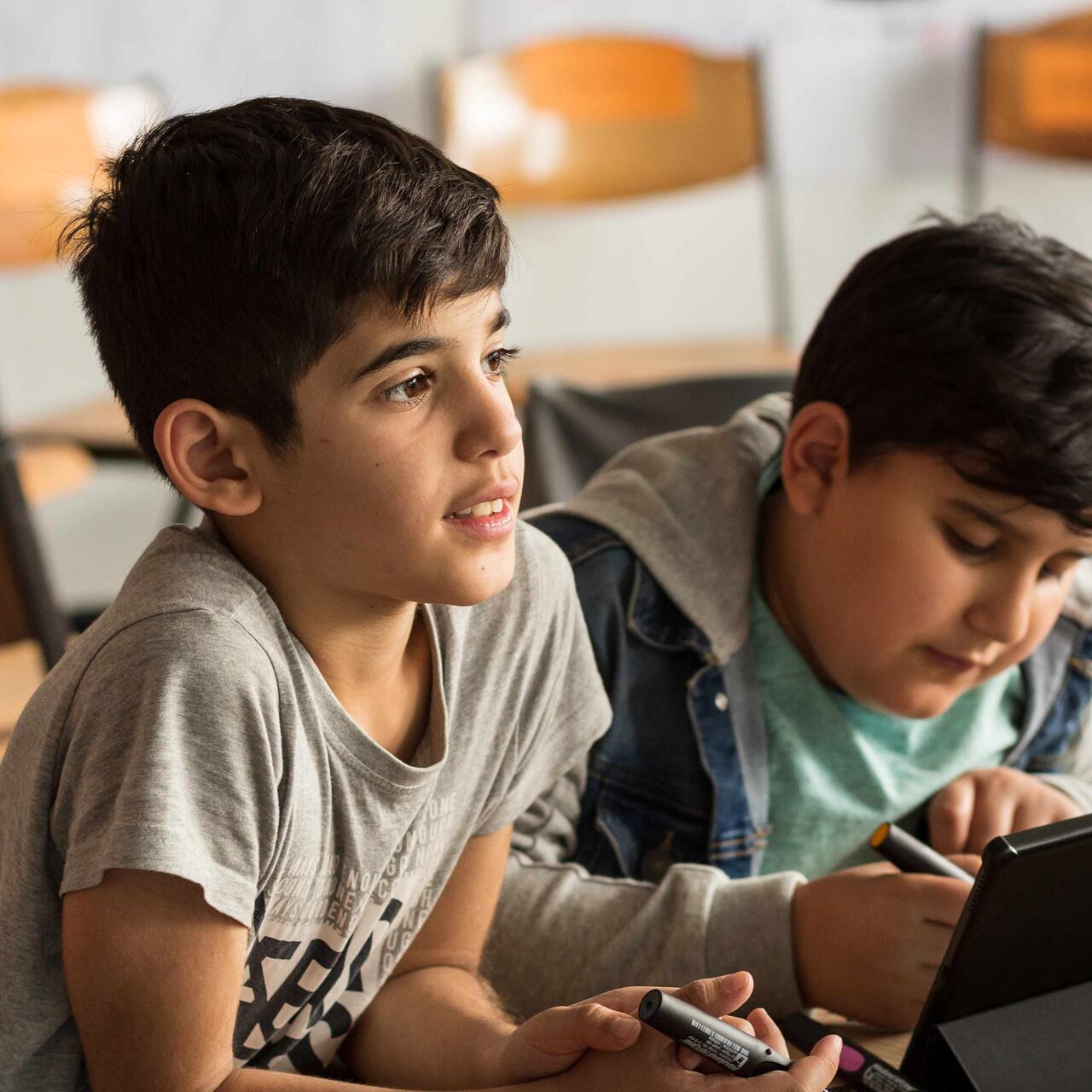 Zwei Jungs sitzen am Schreibtisch in einem Klassenzimmer.