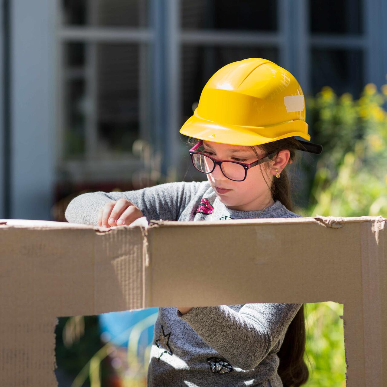Ein Mädchen mit einem gelben Bauhelm bastelt etwas.