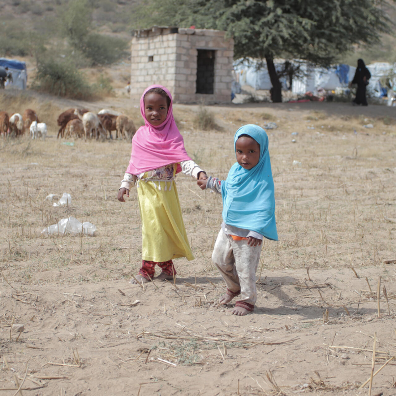 Two young children holding hands, walking in village surroundings