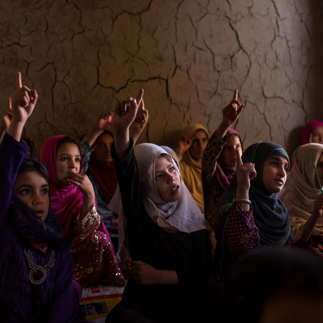 Eine Gruppe von Mädchen in Afghanistan sitzt im Unterricht. Die Mädchen haben ihr Hand erhoben und beteiligen sich an der Schul-stunde