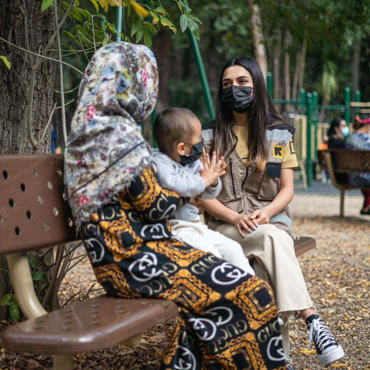 한여성IRC 통역관이멕시코시티놀이터의공원벤치에앉아아기를안고있는아프간어머니와이야기하고있습니다.