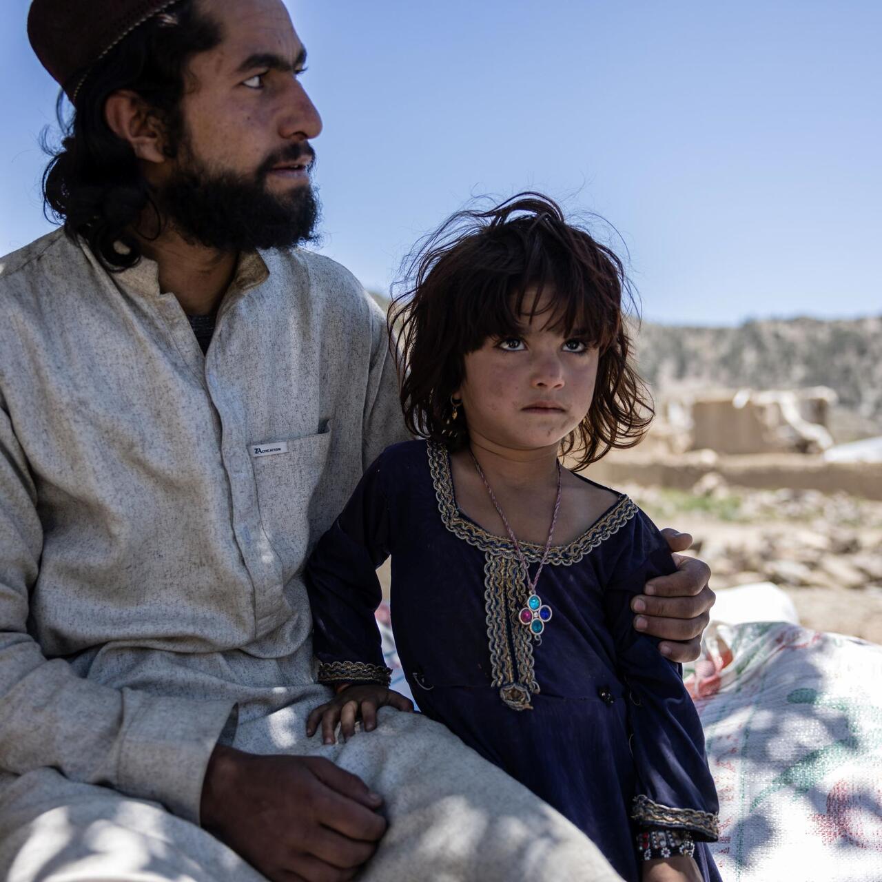 Afghanistan earthquake - An older brother holds his younger sister while looking at the damage to their house