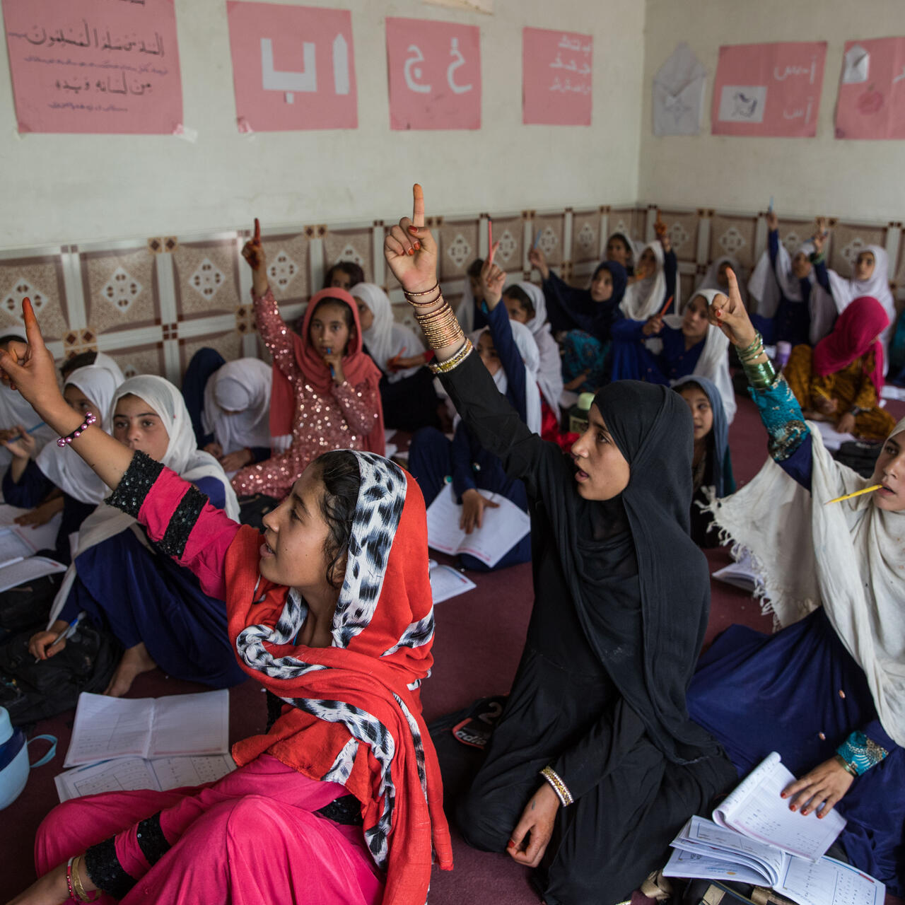 Girls sitting on the floor raise their hands in an IRC community education program in Afghanistan
