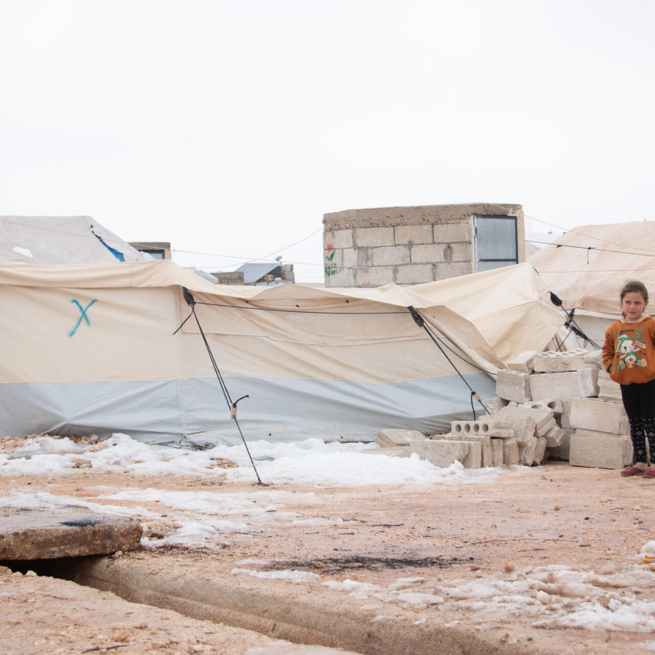 Little girl standing in front of her family's makeshift tent in a refugee camp in Syria.