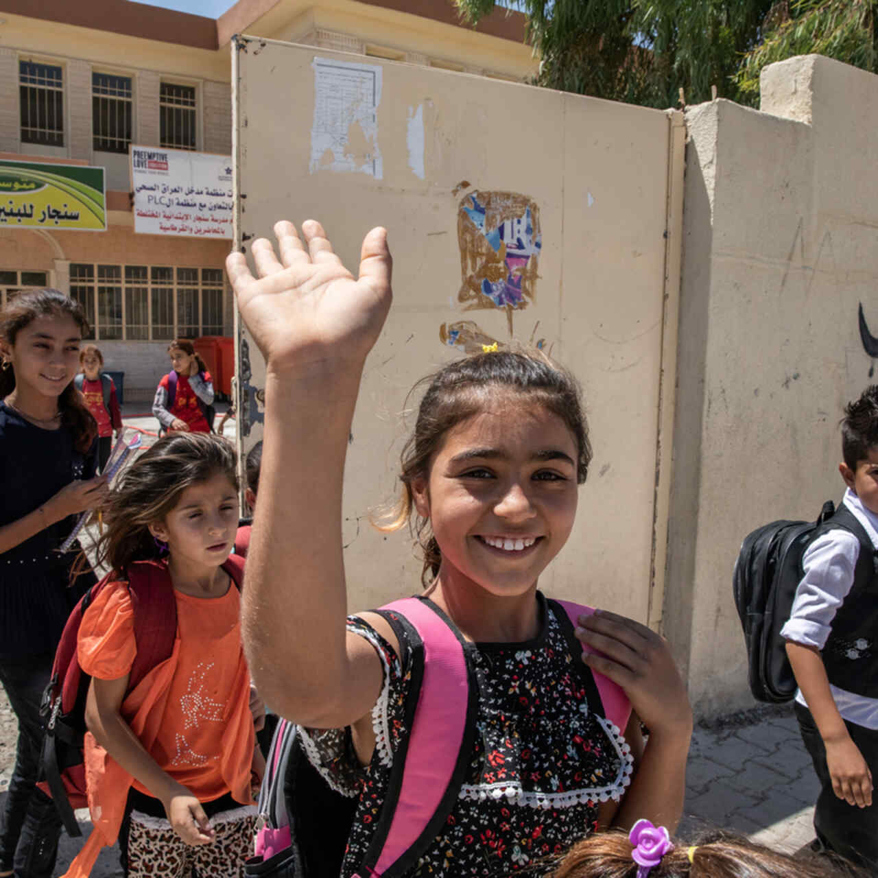 Darin, en ung flicka från Sinjar, Iraq, vinkar utanför sin skola.