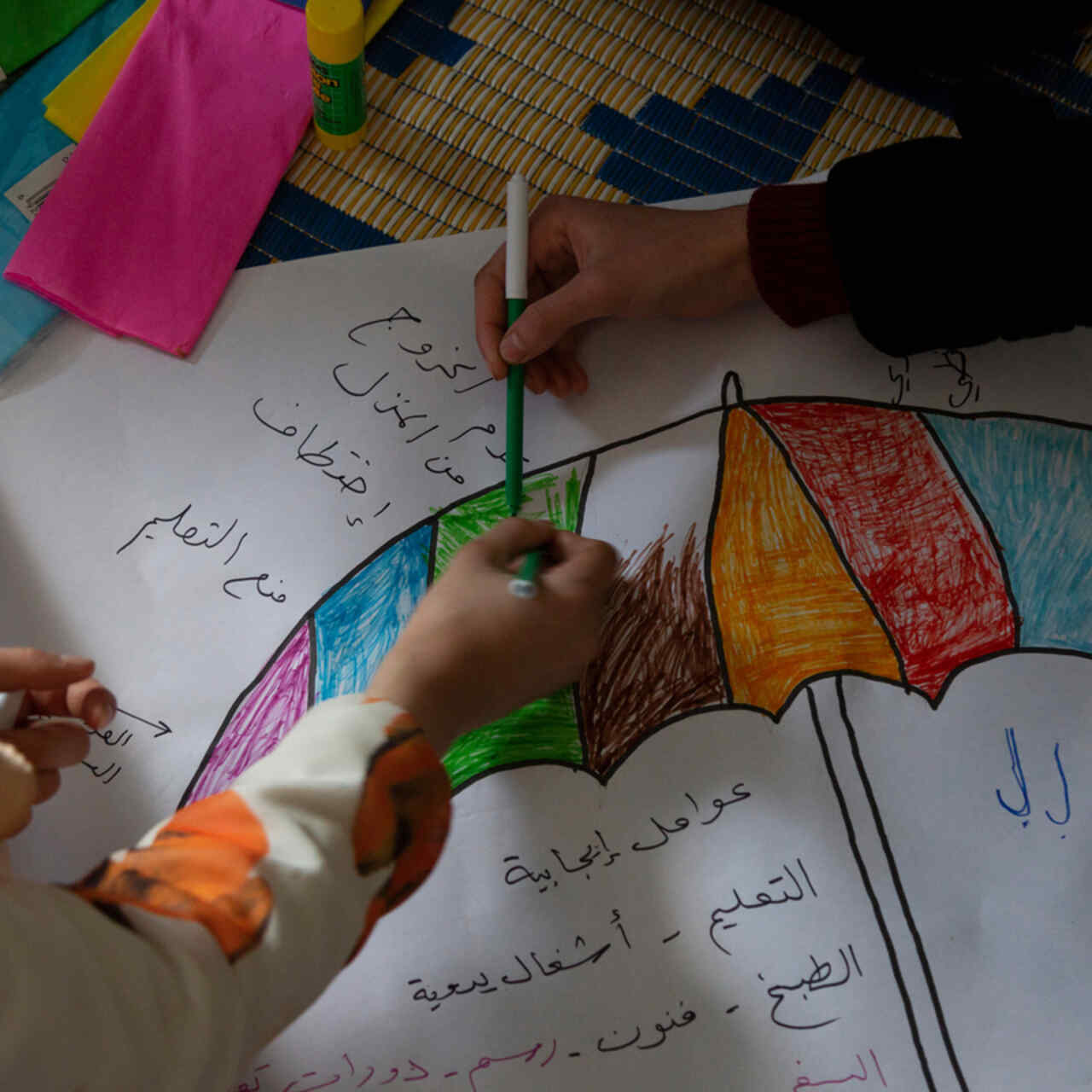 Syrian refugee girls color and write on a piece of paper on the floor in the safe space where they take part in different kind of activities with the IRC WPE team.