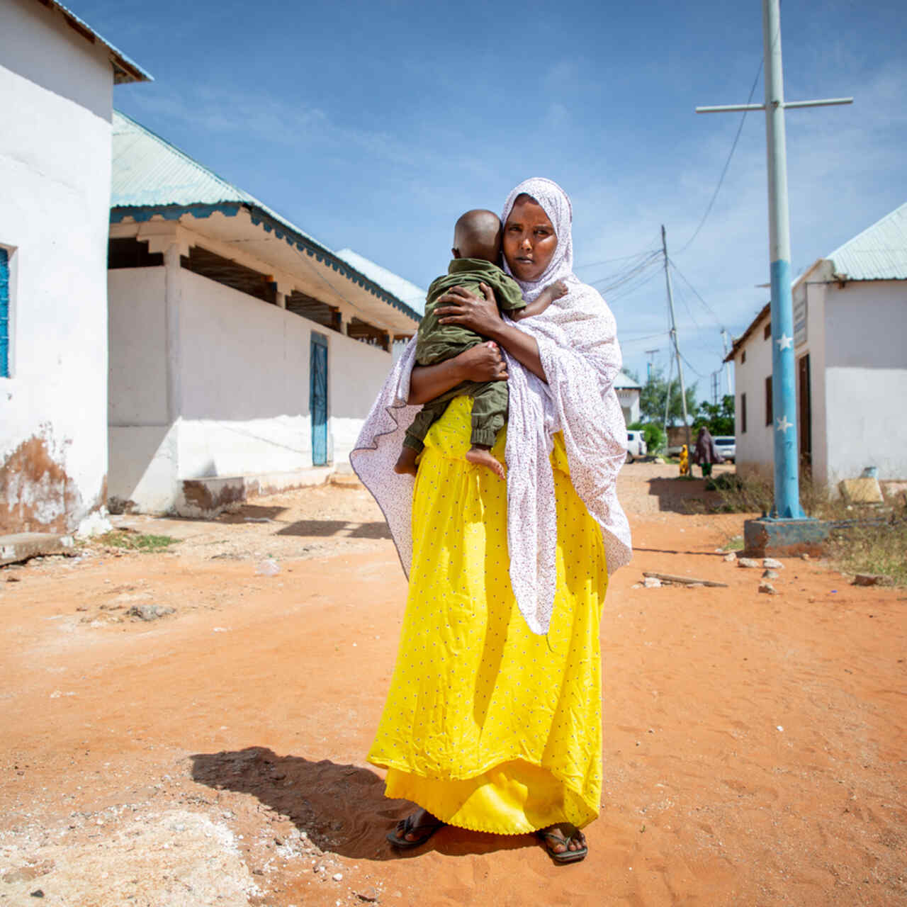 Fartun stands in the street, holding her baby son.