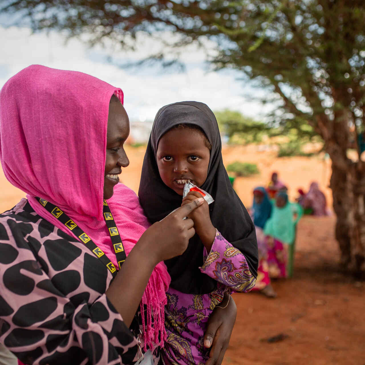 IRC staff with young girl eating PlumpyNut in Olol Village, Somalia