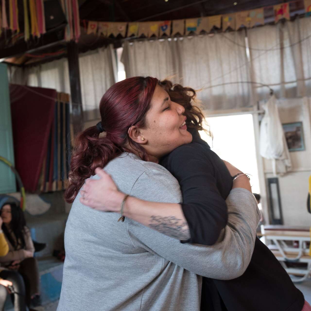 Zwei Frauen umarmen sich in einem Raum voller Menschen.