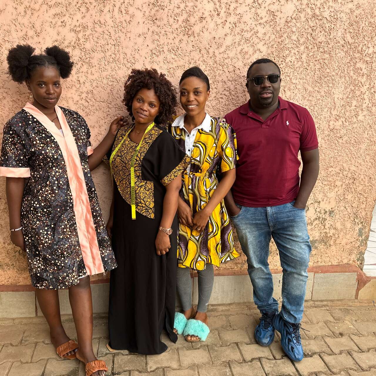 Prince stands against next to three tailors while on a visit back to Uganda.