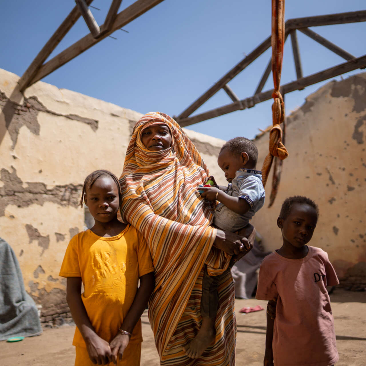 En familj i Sudan står vid sin bostad som saknar tak.