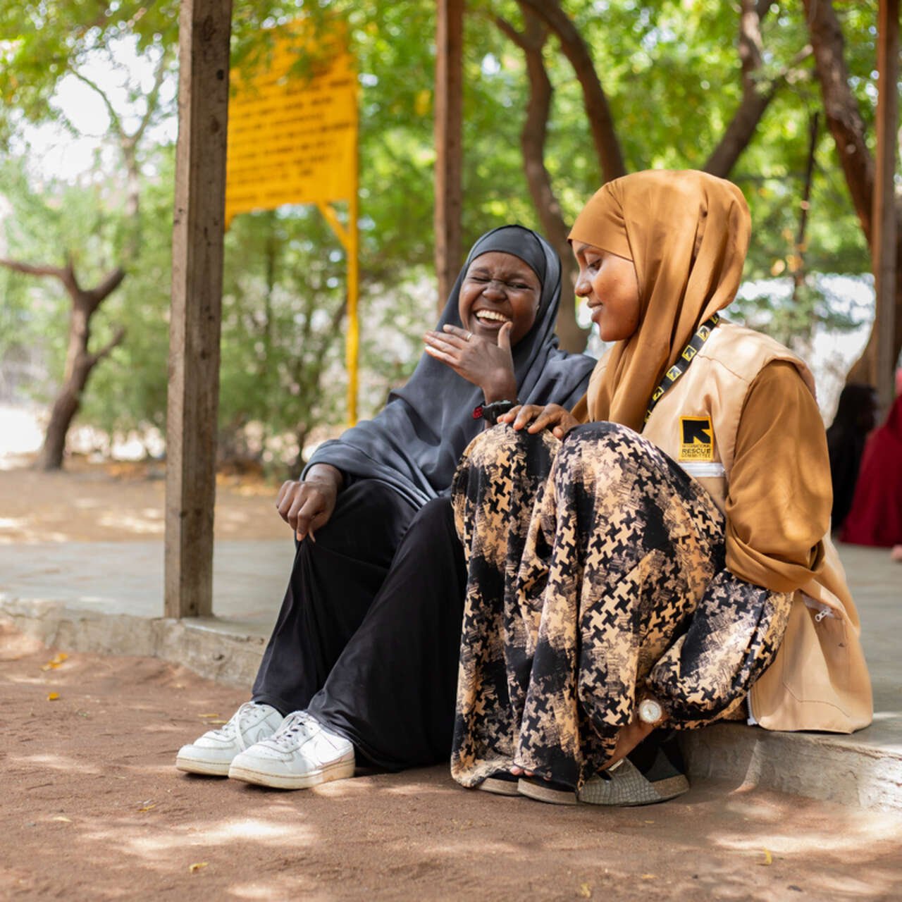 Två av RESCUE:s kvinnliga medarbetare sitter ner och pratar i skuggan.