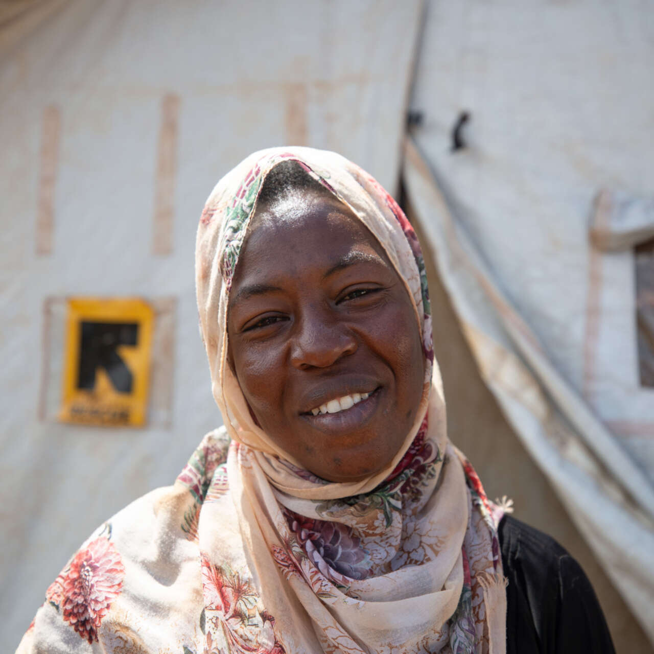 Kvinna i Uganda ler mot kameran, i bakgrunden syns RESCUE:s logga.